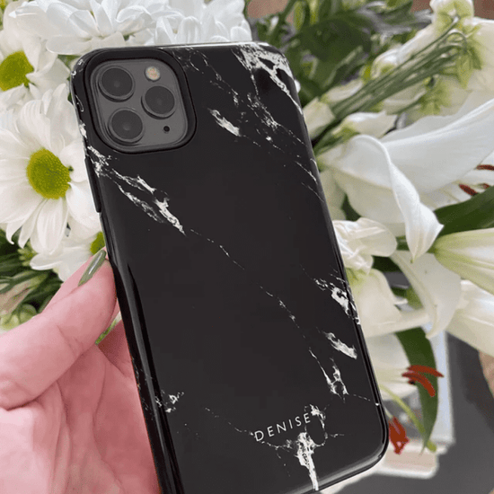 Black marble phone case with the name Denise on being held up against white flowers