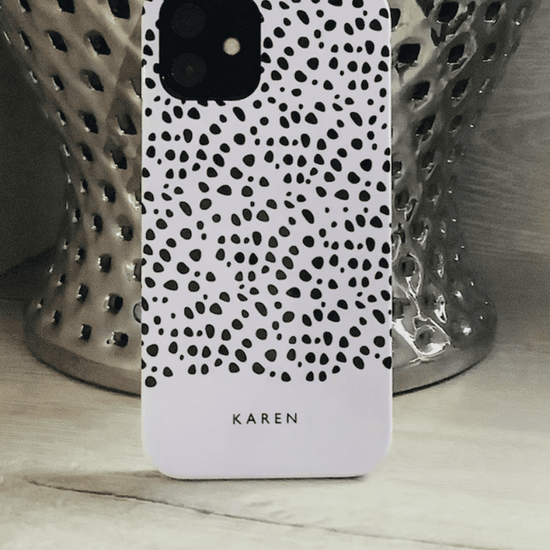 Black dots on white phone case with the name Karen personalised at the bottom in front of a silver vase